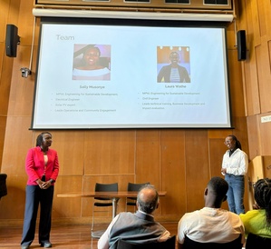 Two female students making a presentation, with their presentation projected on the screen in the background.